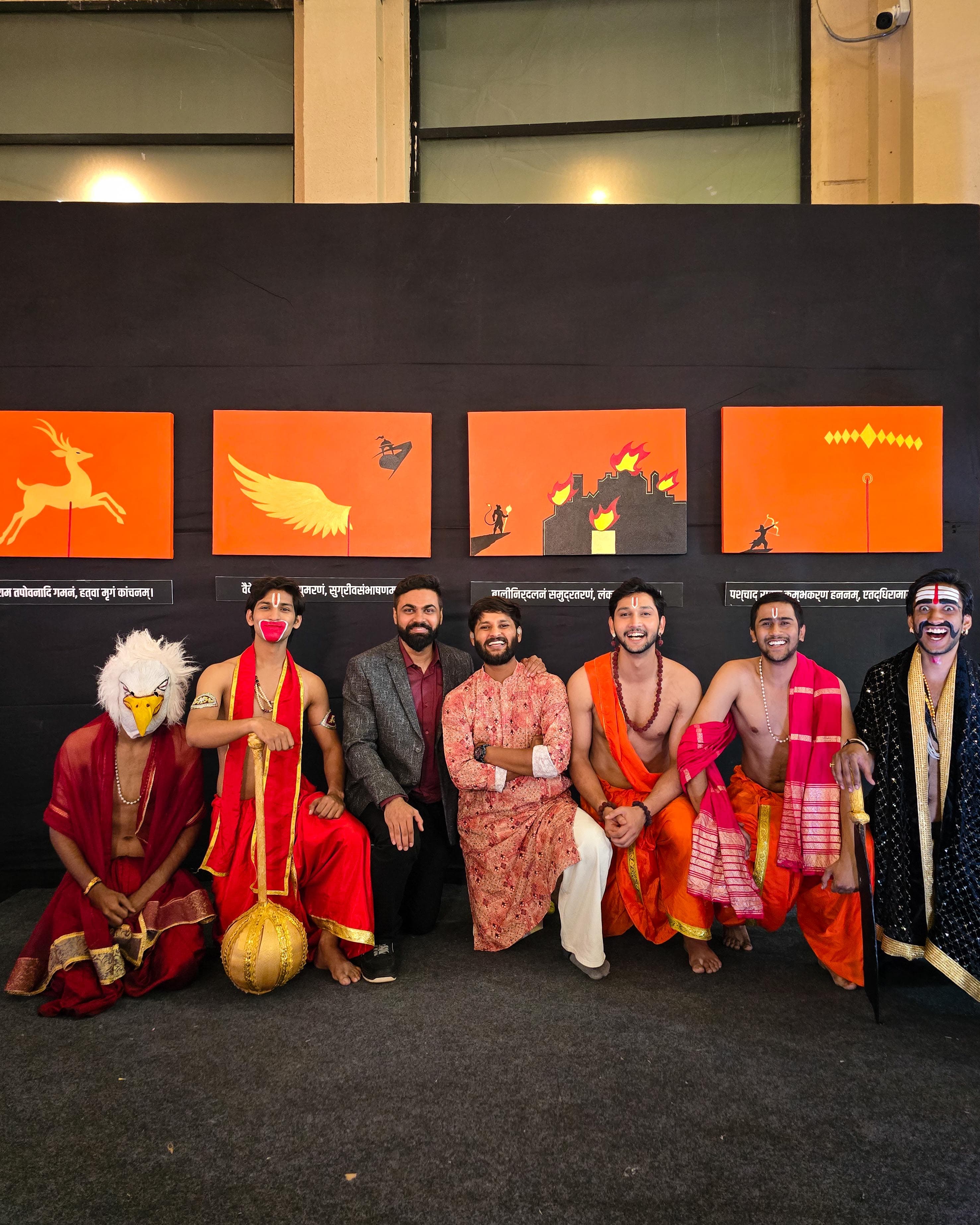 Performers seated below a row of orange narrative artworks